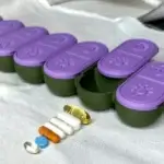 Purple lid pill organizer displayed with pills beside it on a soft white fabric