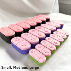 A comparison photo of the 3D-printed pill box in three sizes—Small, Medium, and Large. All sets are displayed side-by-side in pastel pink lids with different colored bases, showing the difference in length, width, and depth. Each pill box features engraved sun and moon symbols with smooth sliding lids. The image helps customers visually compare sizes before choosing the best option.