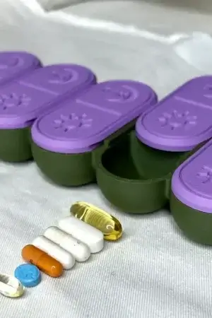 USACUTTIE 3D printed pill box with a row of white, orange and gold supplements laid out beside the open compartment