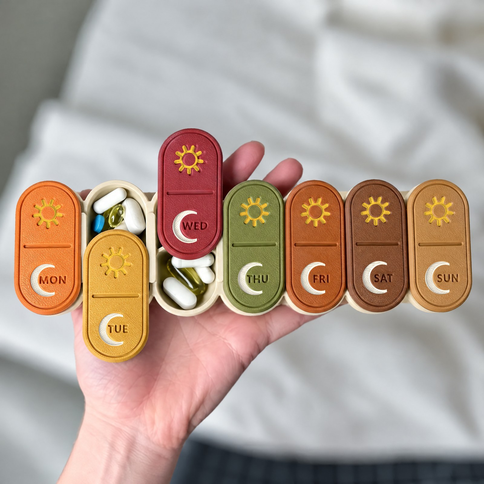 Fall 7-day pill organizer held in one hand, showing sun and moon icons on every lid