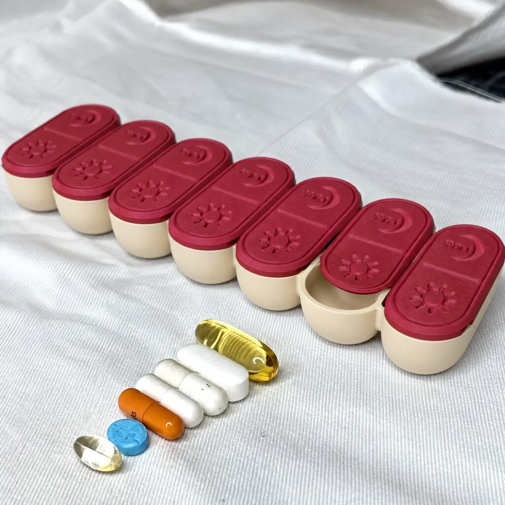 Cute weekly pill organizer with cranberry red sliding lids and colorful pills beside it